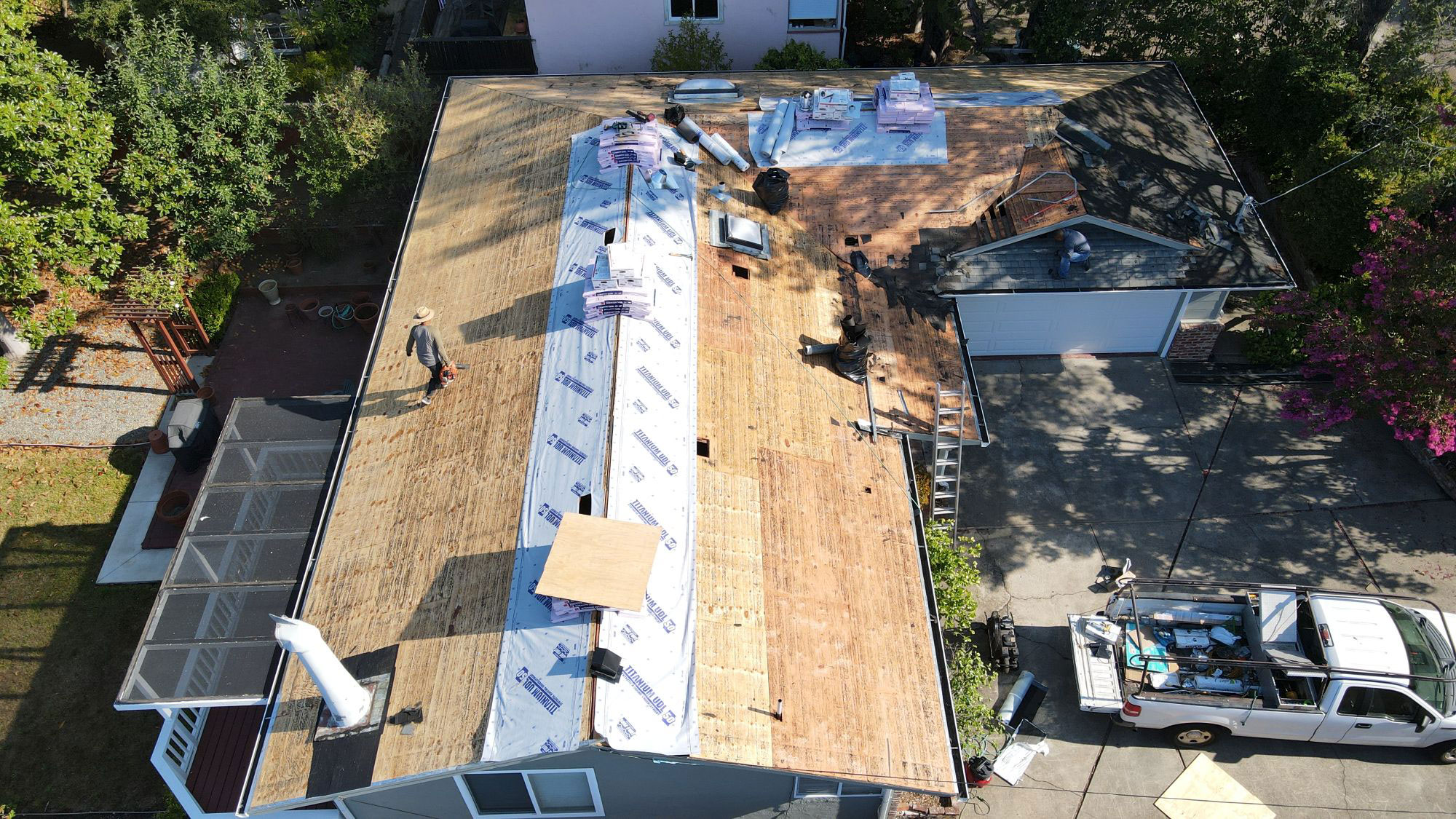 The image shows a roofing construction site with tarps covering sections of the roof, indicating ongoing work on a house.