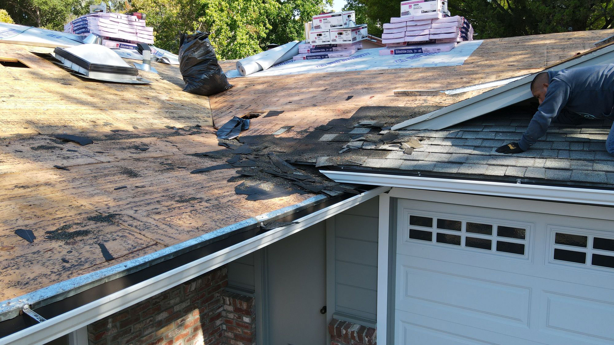 The image shows a house with a partially completed roof under construction, with visible tarps and materials on the ground.