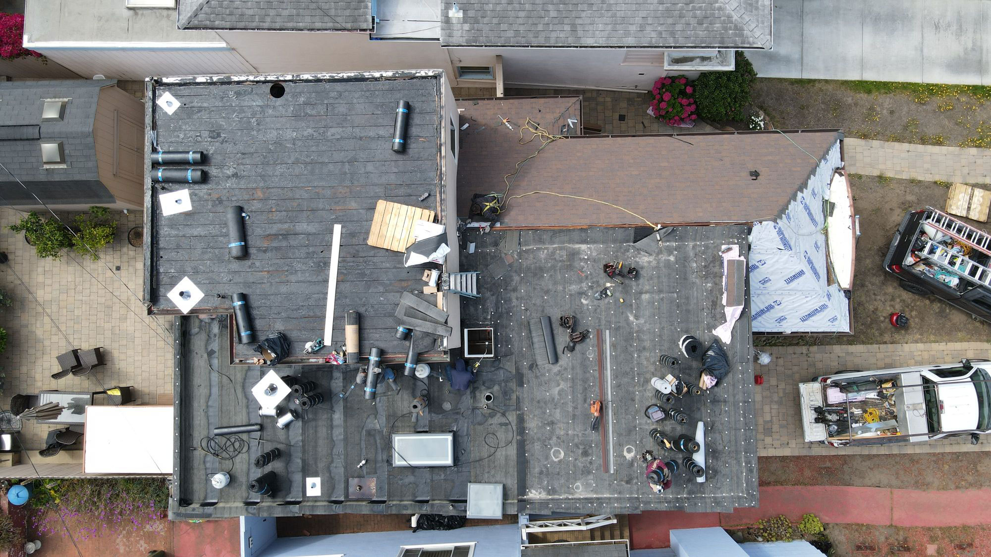 The image shows a house undergoing renovation with a visible roof repair and construction materials scattered on the ground around it.