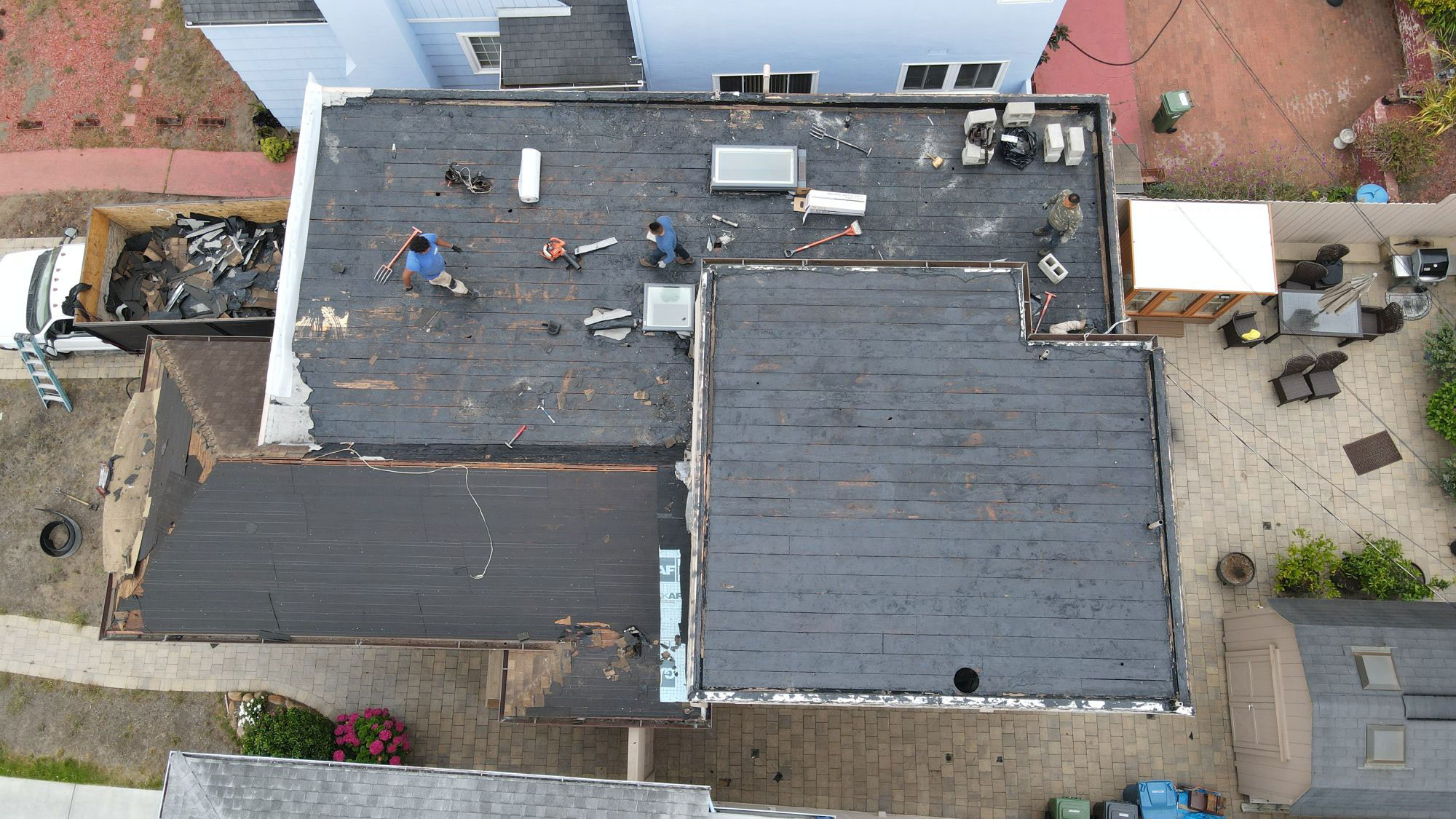 The image shows a house undergoing roof repair with workers on the ground and scaffolding set up around the roof area.