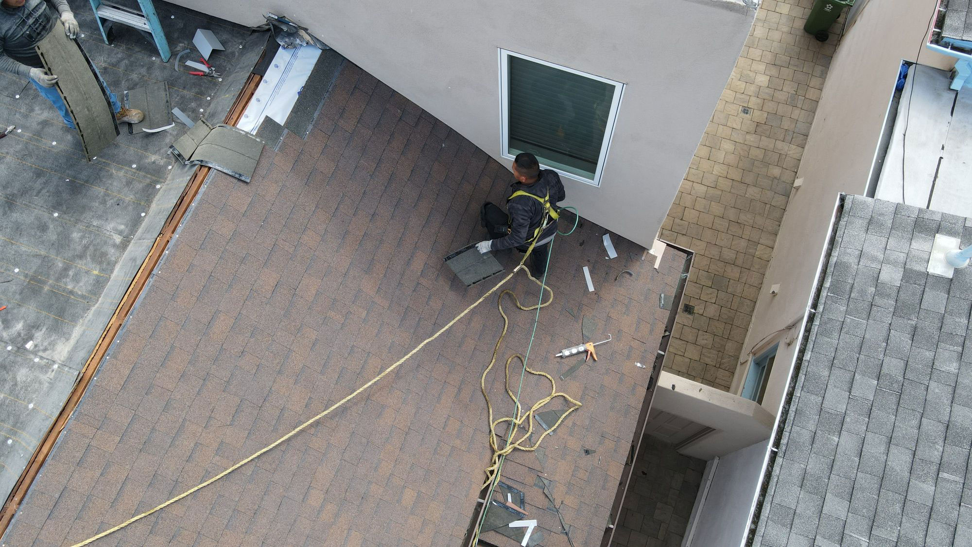 The image shows a person working on a rooftop, laying out a hose while standing next to a brick patio area.