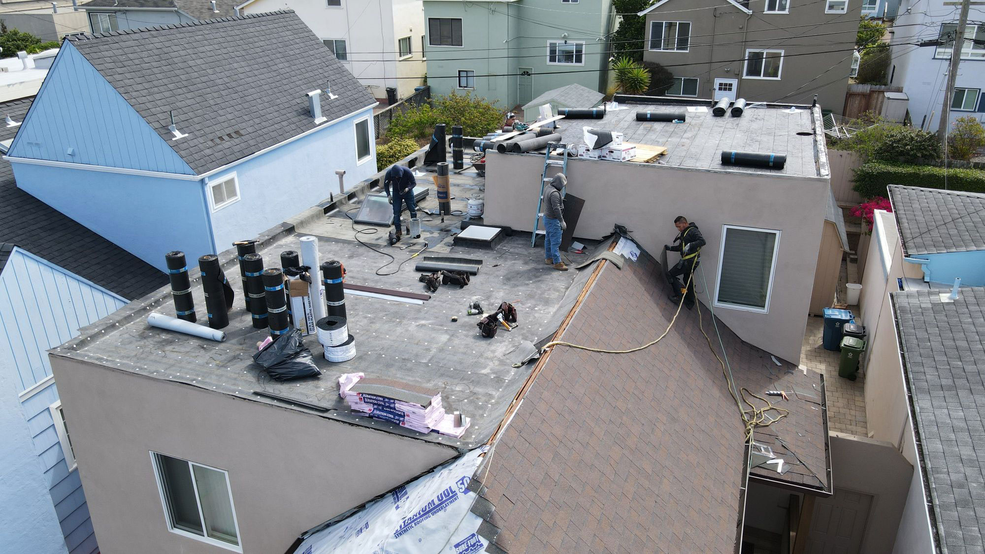 The image shows a residential building under construction with exposed roofing materials and workers on site.