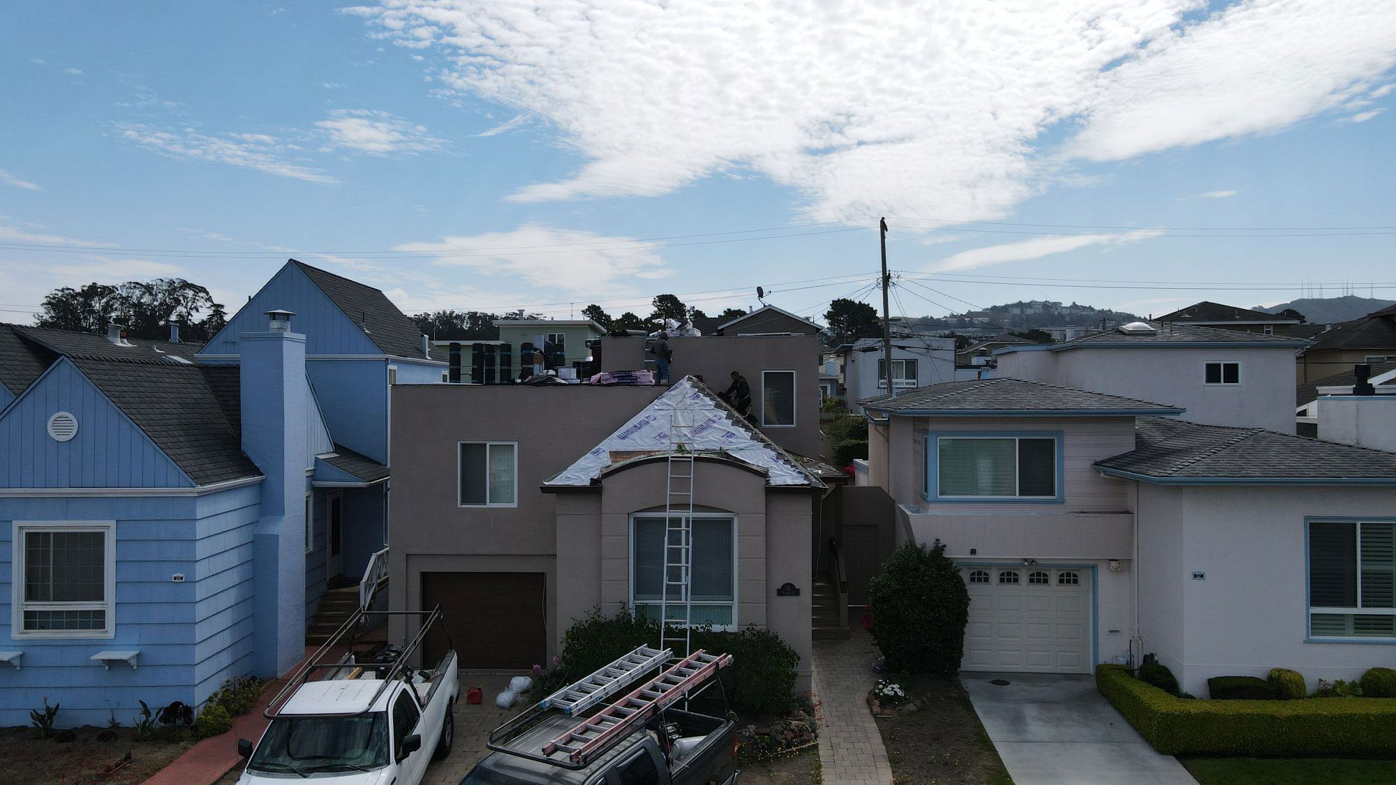The image shows a residential neighborhood with houses and vehicles parked on the street, under a clear blue sky.