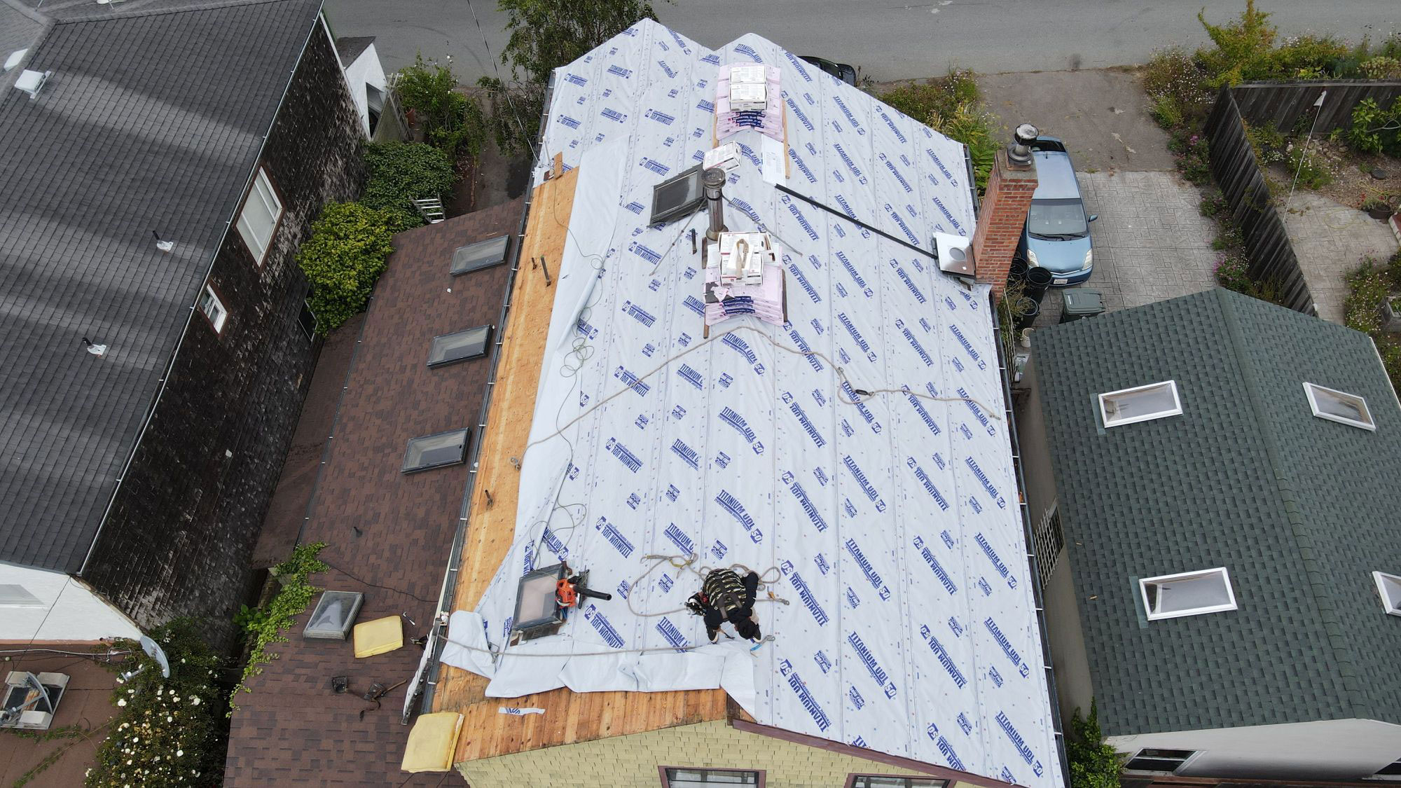 A house under construction with a roof covered in protective sheeting, viewed from an elevated angle.