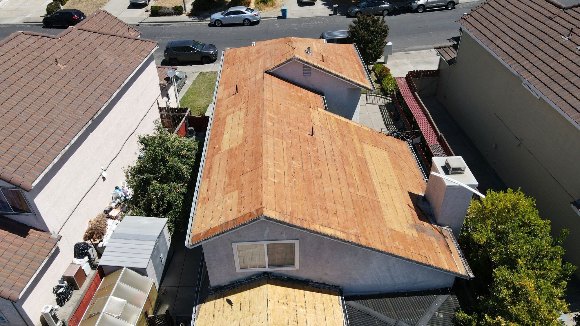 The image shows a residential house with a flat roof under construction or renovation, featuring visible wooden planks and metal flashing materials on its surface.