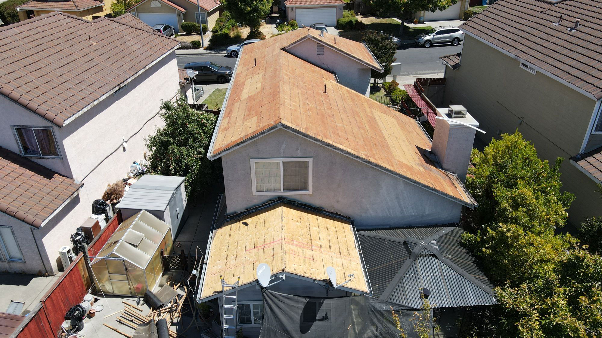 The image shows a house undergoing roof construction with visible wooden planks on top of the existing roof, indicating ongoing work.