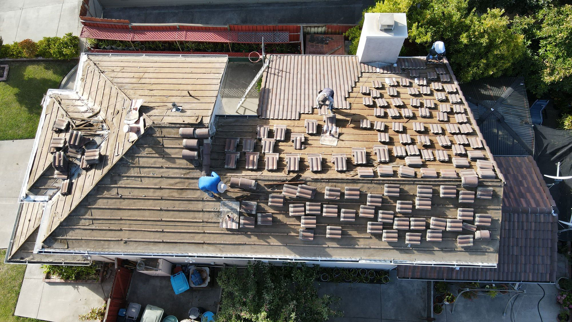 The image shows a residential rooftop under construction with workers on site, surrounded by scaffolding and materials, indicating an ongoing renovation project.