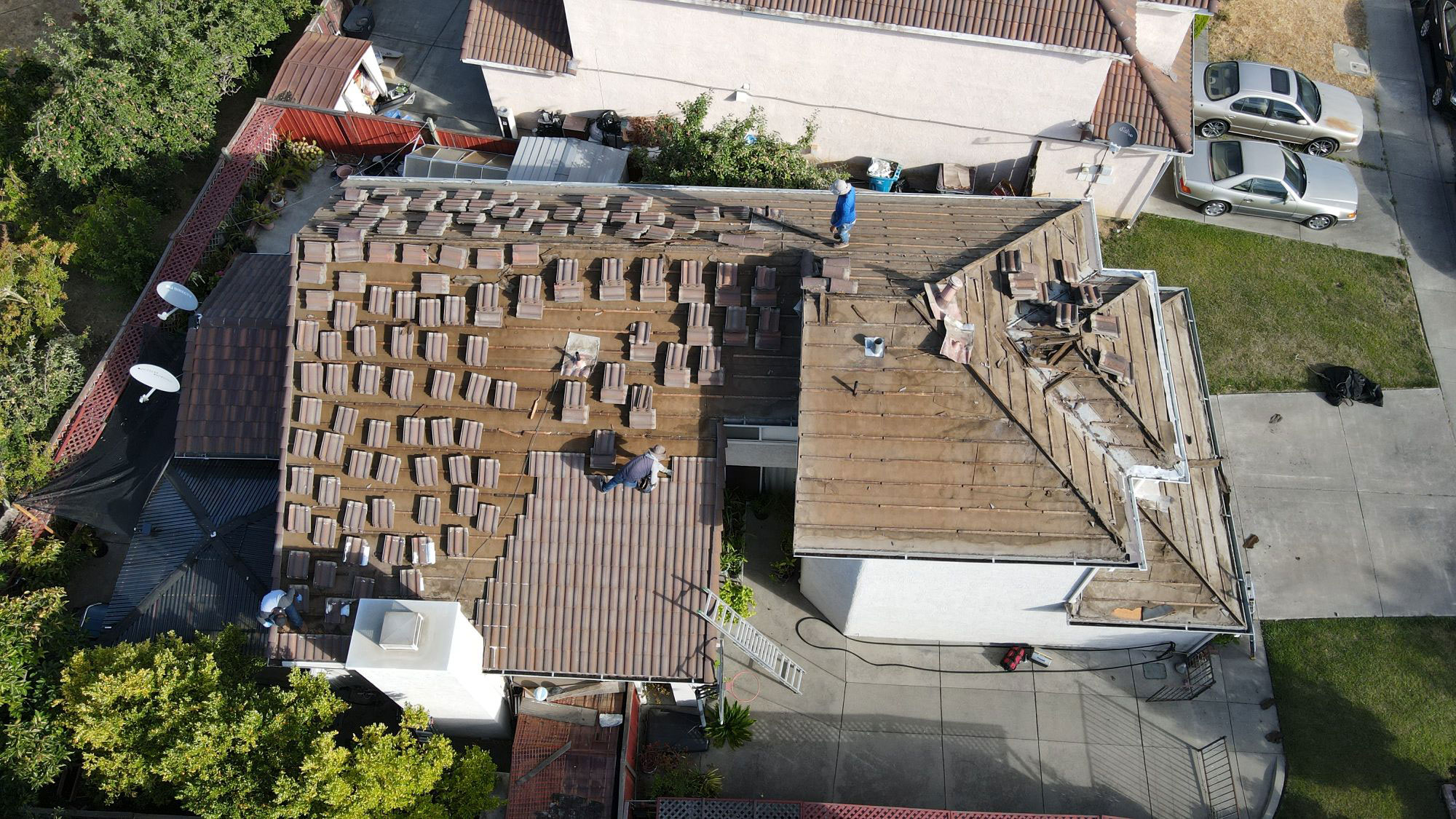 The image shows a house with a damaged roof under repair, featuring multiple shingles removed and replaced, set against a clear sky.