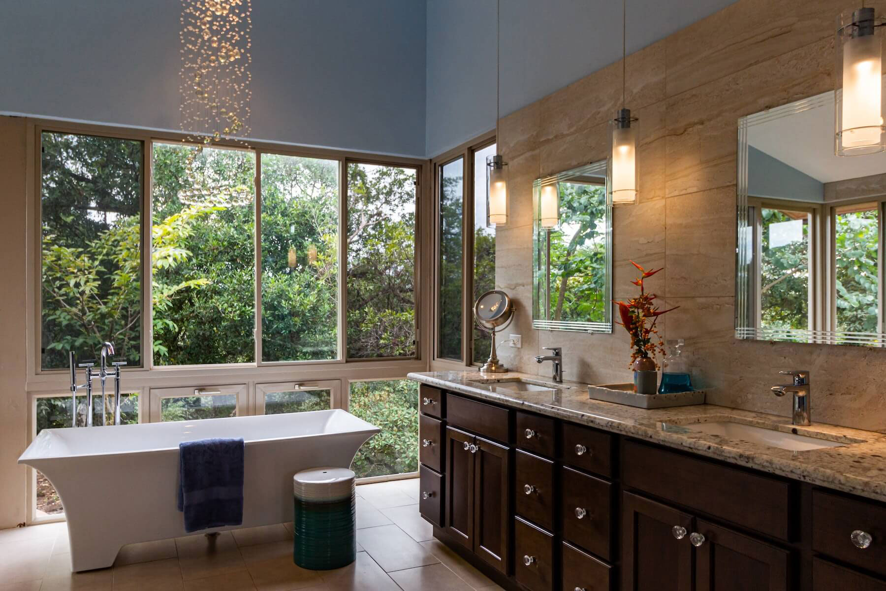An interior view of a modern bathroom with large windows, a soaking tub, double sinks, and a spacious design.