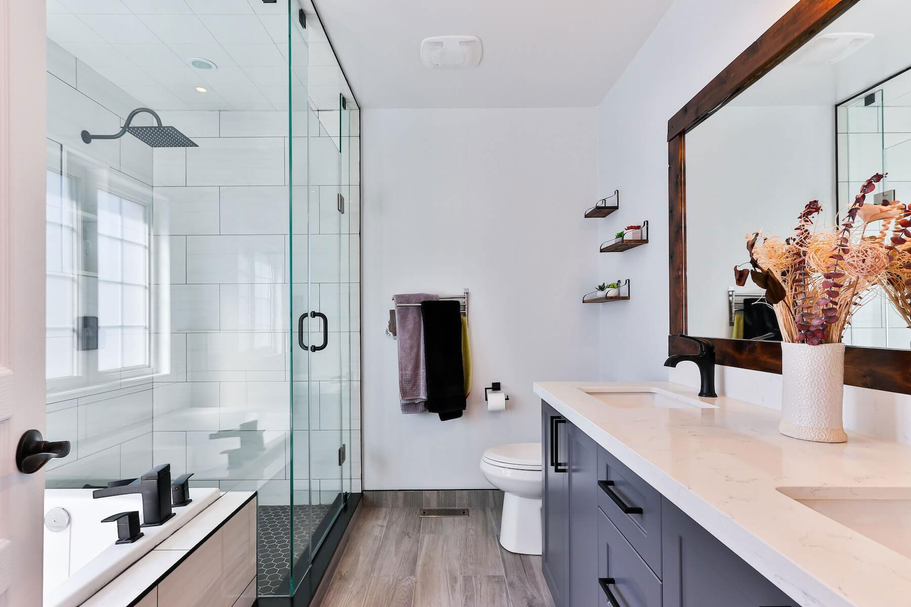Modern bathroom with glass shower door, white tiled walls, black fixtures, and contemporary design.
