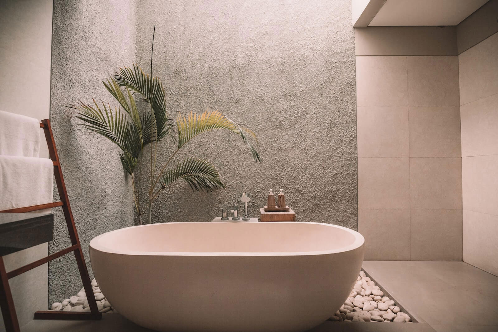 The image depicts a modern bathroom interior with a large round bathtub, a potted plant, a towel rack, and tiled walls.