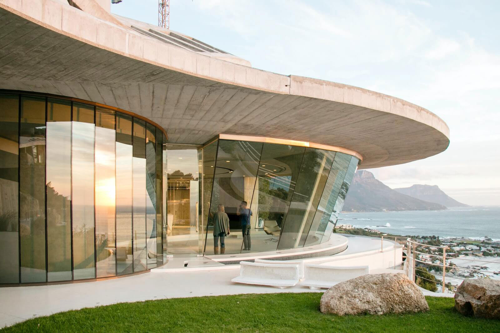 The image shows a modern architectural building with curved glass facades and a panoramic view of the ocean, featuring a contemporary design with a blend of geometric shapes and natural light.
