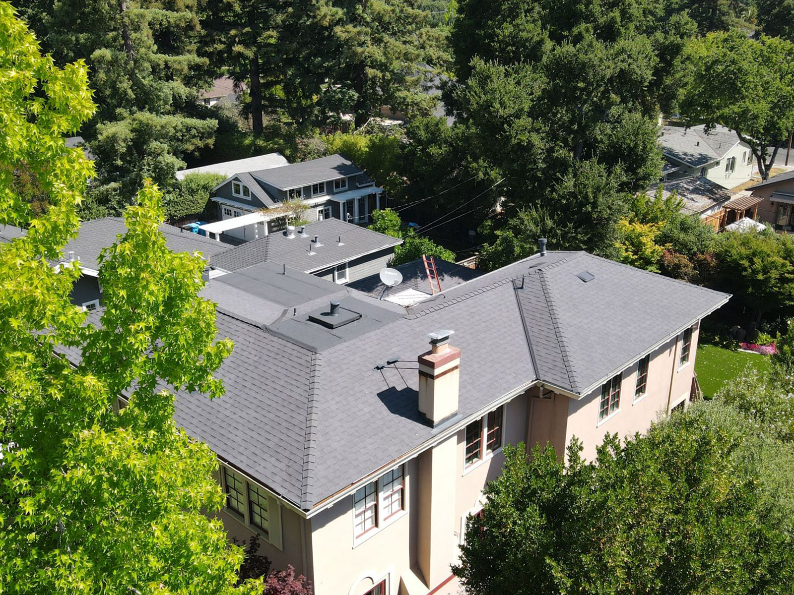 The image shows a two-story residential building with a gray roof, surrounded by trees and greenery, under a clear sky.