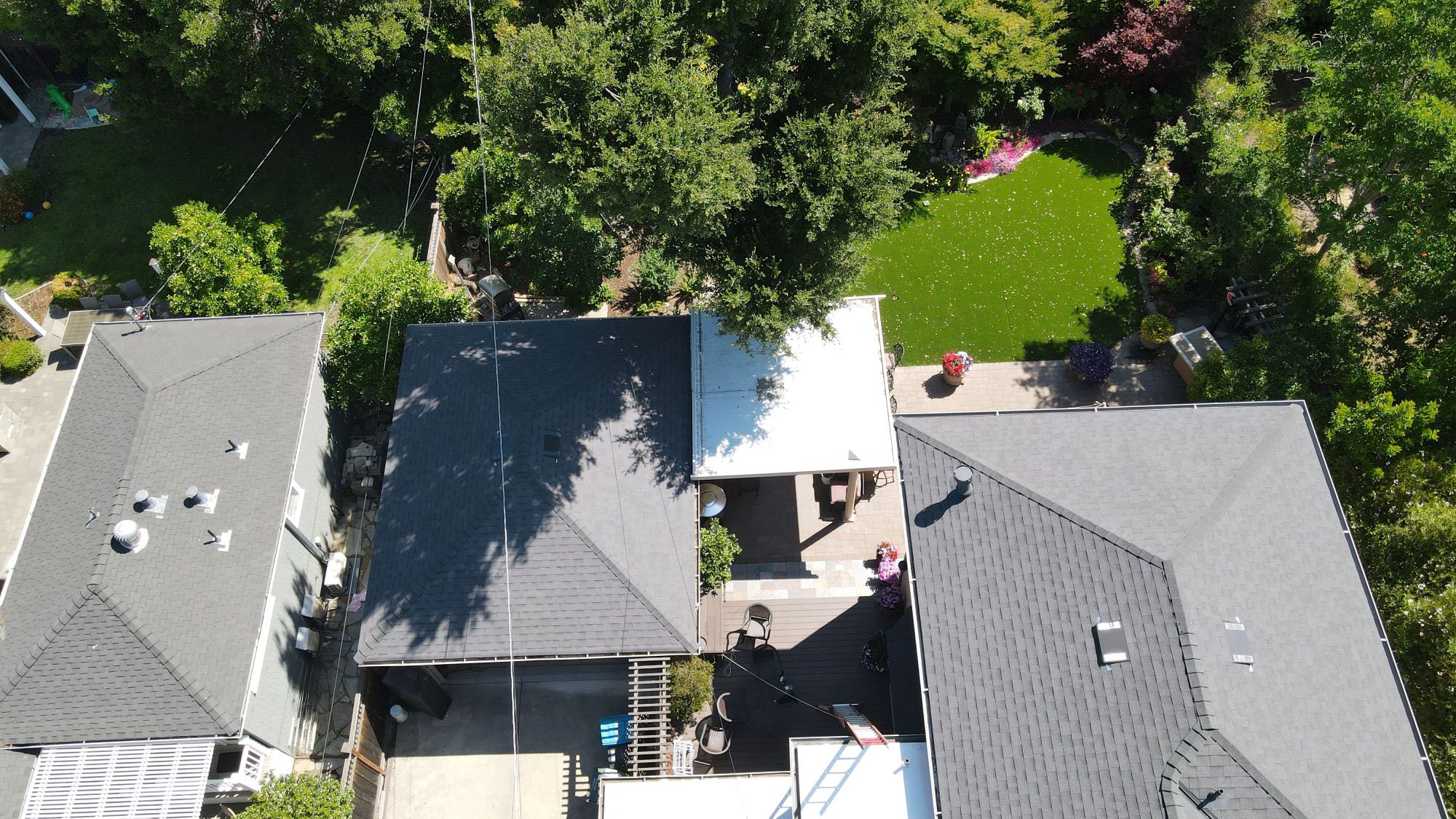 The image shows a two-story residential house with a black shingle roof, surrounded by a fenced backyard.