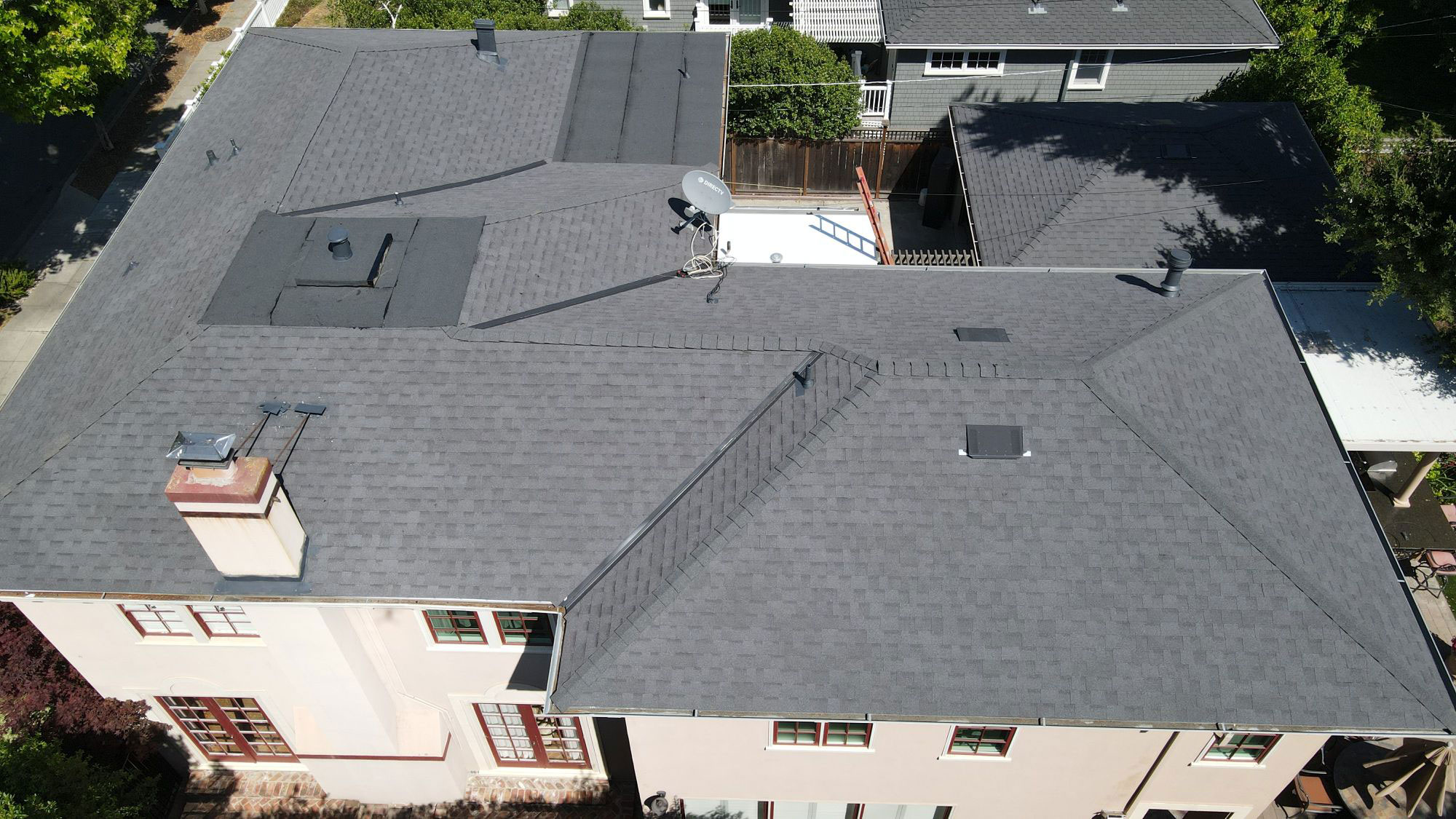 The image shows a residential building with a gray shingle roof featuring multiple vents and a prominent skylight, set against a clear sky.