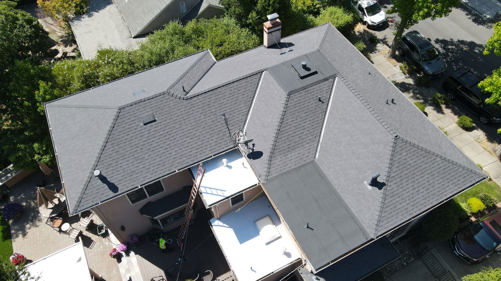The image shows a residential property with a gray roof, undergoing construction or renovation, featuring an attic ventilation system visible on the roof.