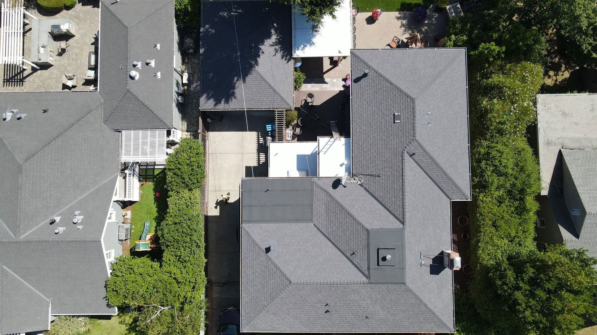The image shows an aerial view of a residential area with multiple houses featuring different roofing materials and colors, including shingles and tiles.