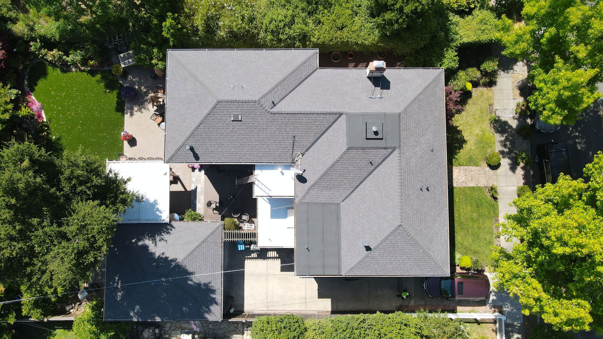 A single-story house with a shingled roof, featuring an angled design and a prominent front gable, set against a backdrop of trees.