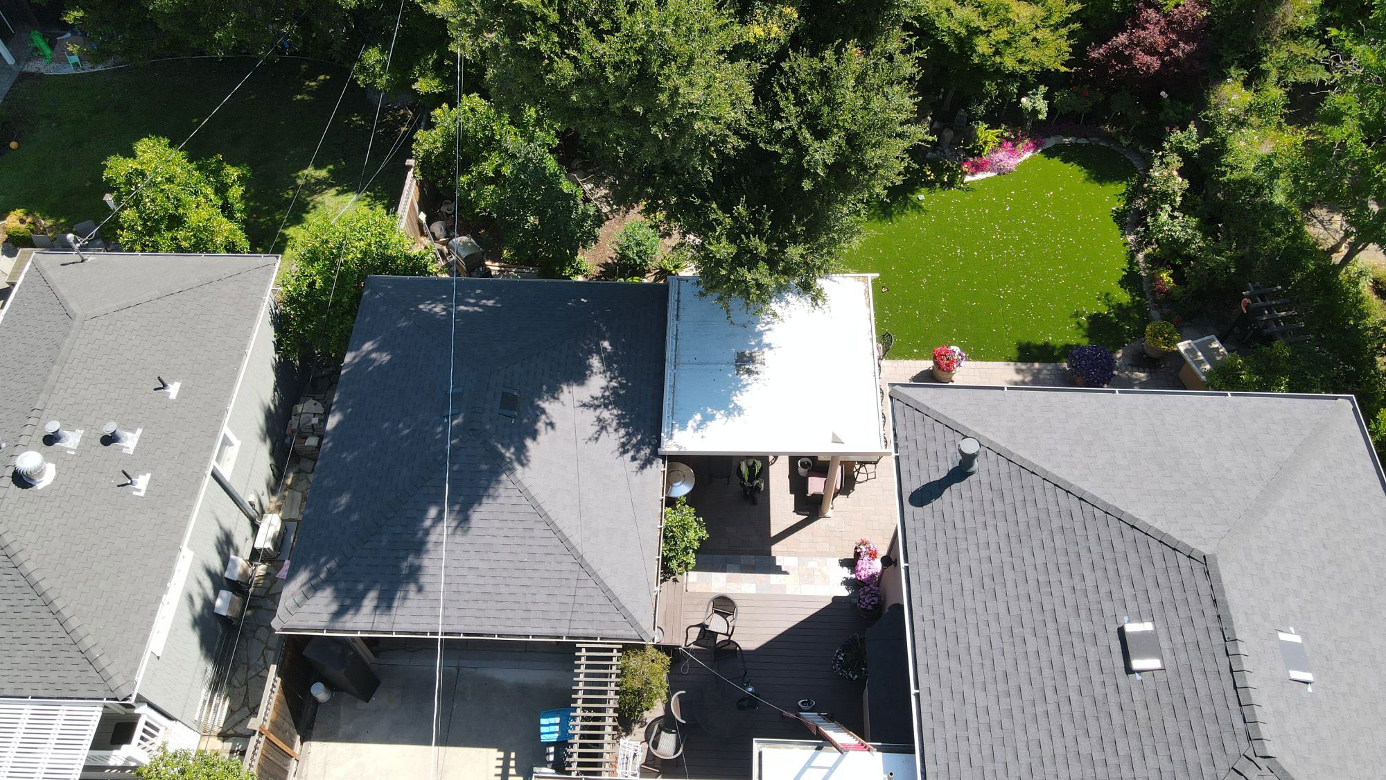 The image shows a residential area with several houses featuring different roofing materials, including shingle and tile, set against a clear sky.