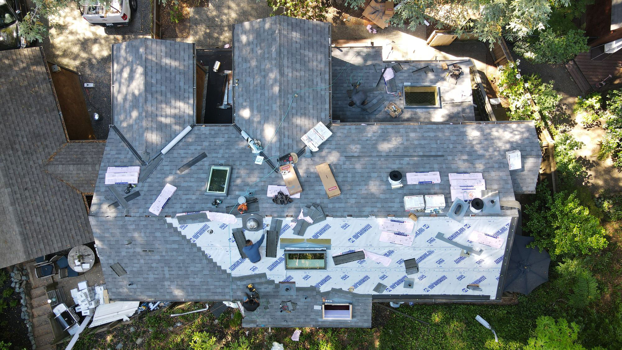 The image shows a house with its roof partially removed, revealing exposed rafters and insulation, indicating ongoing construction or renovation work.