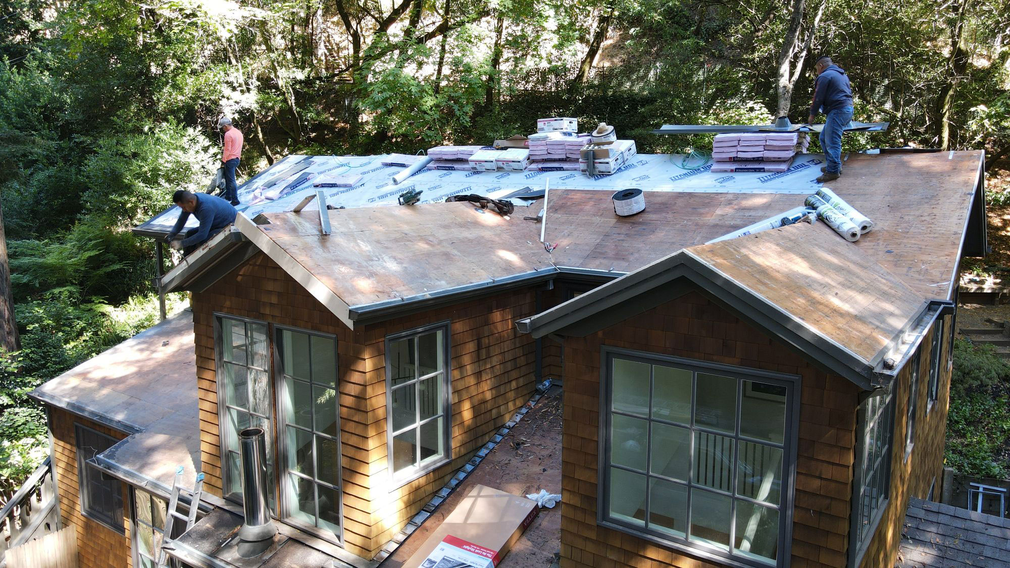 A house under construction with workers on the roof installing shingles.