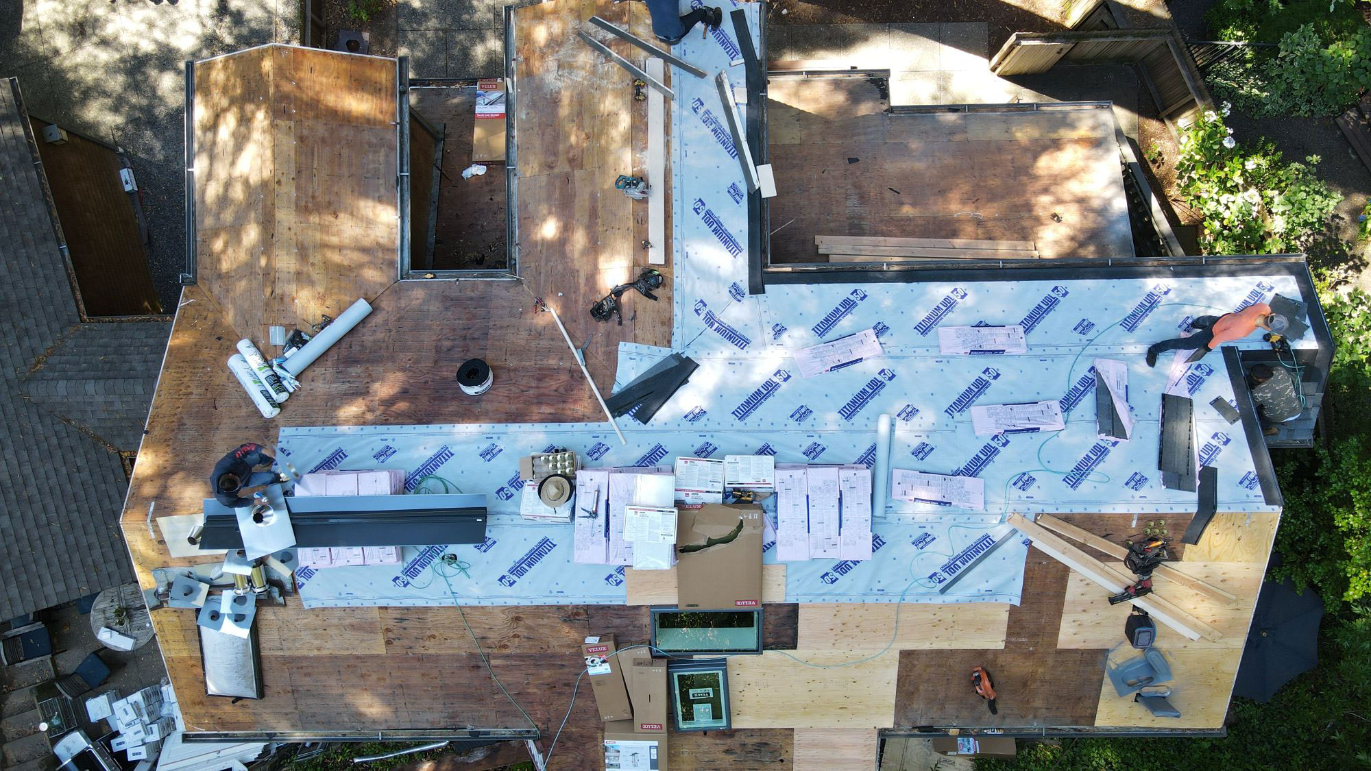 The image shows a house under construction with exposed wooden studs and a partially installed roof covered with construction materials.