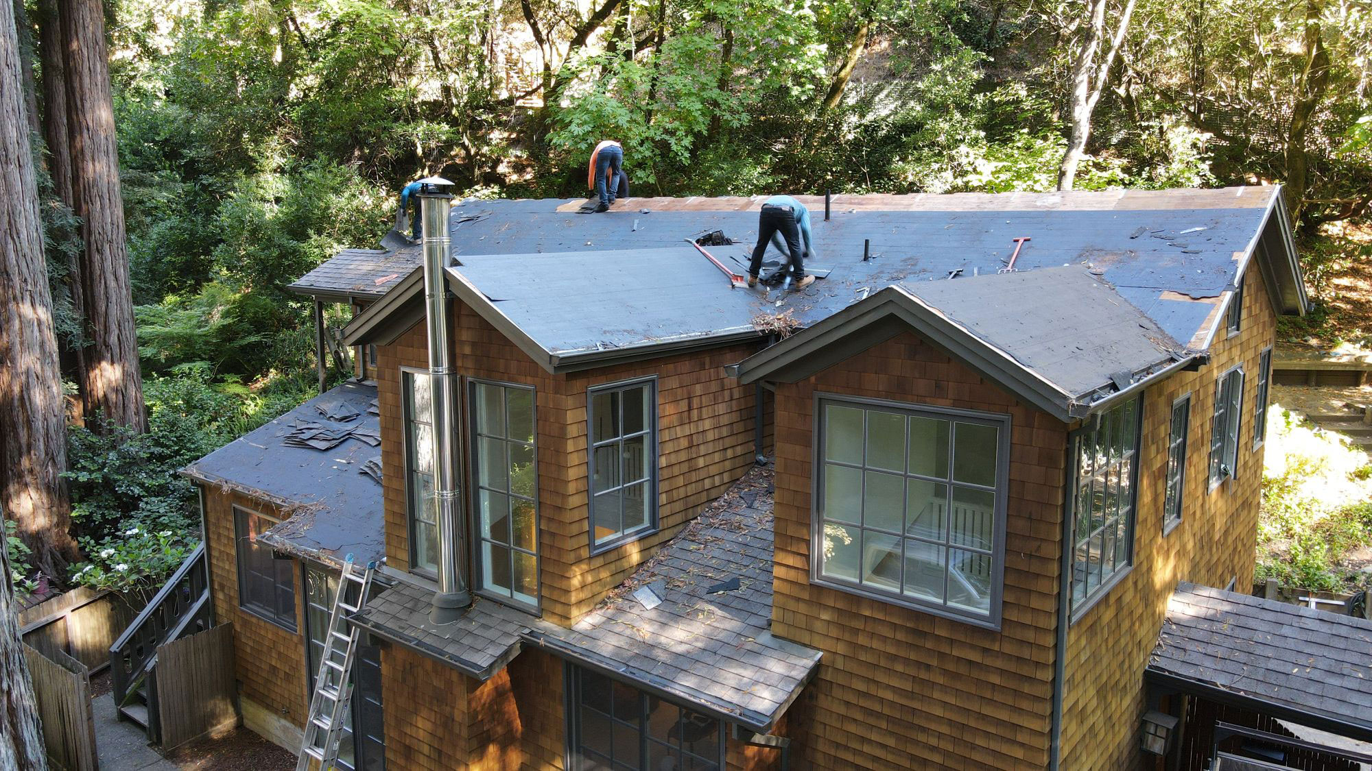The image depicts a residential house undergoing roofing work, with a person working on the roof and visible signs of construction activity.
