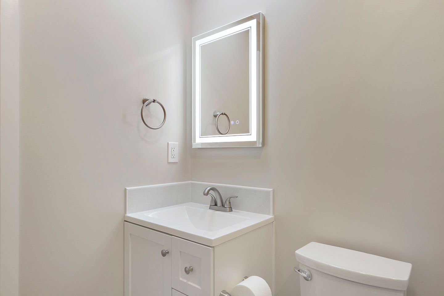 The image shows a bathroom with a white sink, a small mirror above it, and a toilet visible in the background.