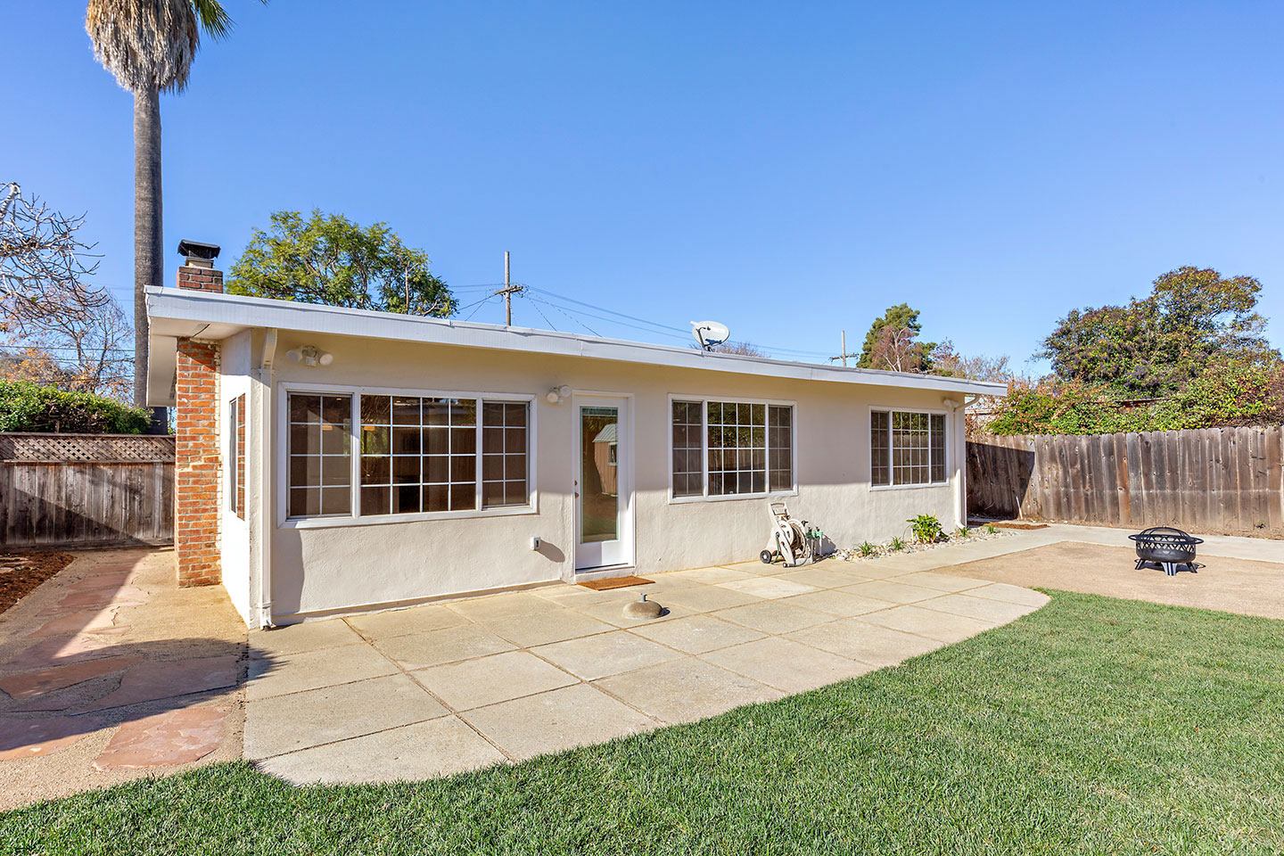 The image shows a single-story house with a flat roof, a front porch, and a garage. It s a sunny day, and the house appears to be well-maintained with a clean driveway.