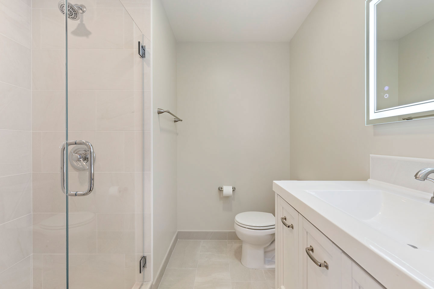 The image shows a modern bathroom interior with a white color scheme, featuring a shower stall with glass door, a white toilet, a white sink with silver fixtures, and a mirror above the sink.