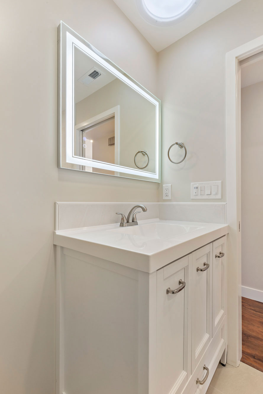 The image shows a modern bathroom with a white sink, a large rectangular mirror above it, and a clean, minimalist design.