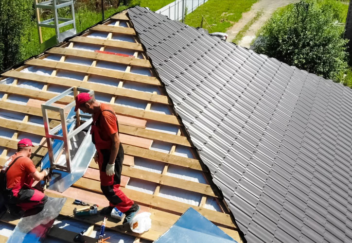 Two construction workers installing roofing material on a building with a partially completed structure.