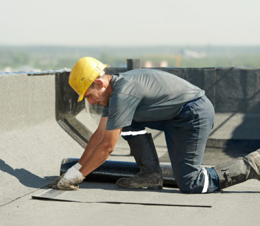 A construction worker kneeling on a roofing project, working with materials.