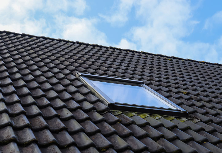 The image shows a close-up view of a window on a roof with black shingles, set against a clear blue sky.