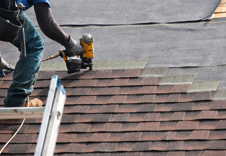 A roofer working on a shingled roof under construction or repair.