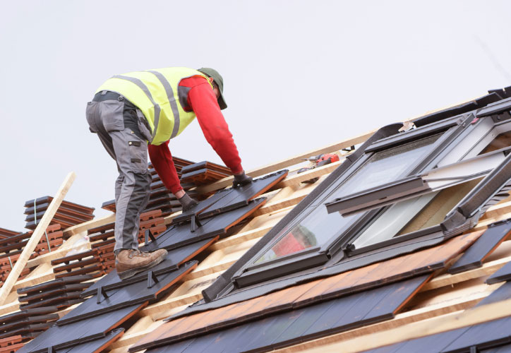 A construction worker standing on a partially built roof during daytime.
