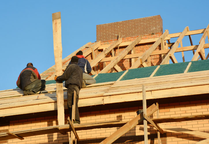 Two construction workers on a roof under construction during daylight with clear skies.