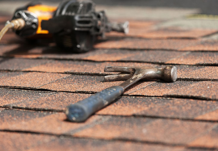 The image shows a close-up view of a rooftop with a hammer lying on its surface, indicating ongoing construction or repair work.