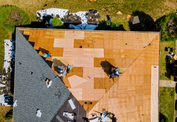 The image shows a roof under repair with visible wooden planks and tarps covering parts of the structure.