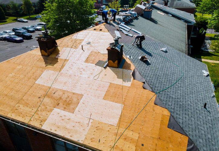 The image shows a rooftop under construction with several workers on site, preparing for the installation of shingles.