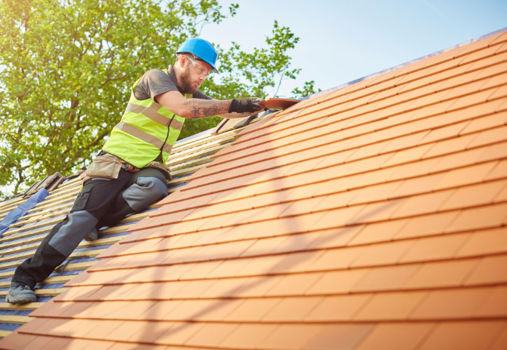 A construction worker repairing a slate roof on a sunny day.