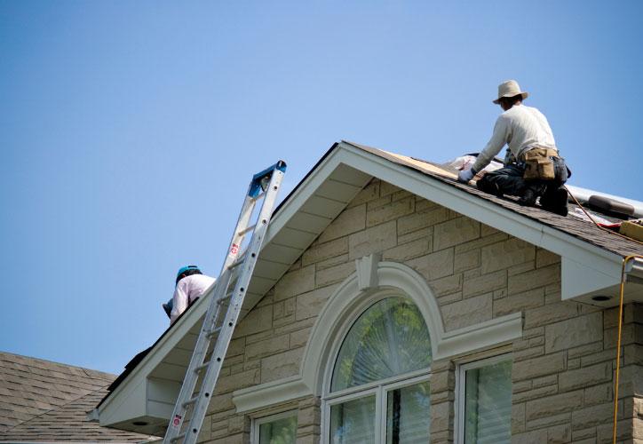 The image shows a person working on the roof of a house during daylight hours.
