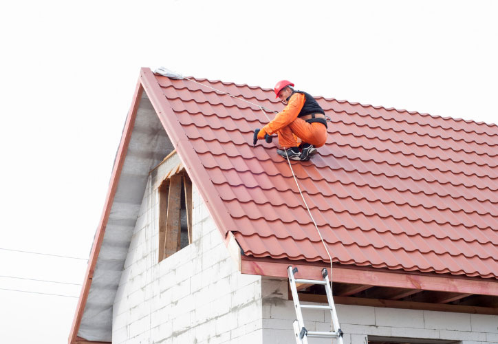 The image shows a construction worker on a roof, installing shingles during daylight.