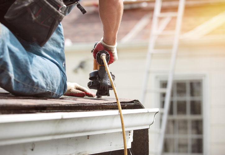 A construction worker using a power tool on a roof during daylight hours.
