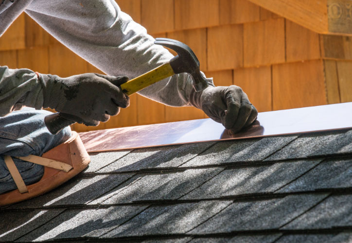 A person working on a roofing project, applying shingles with tools.