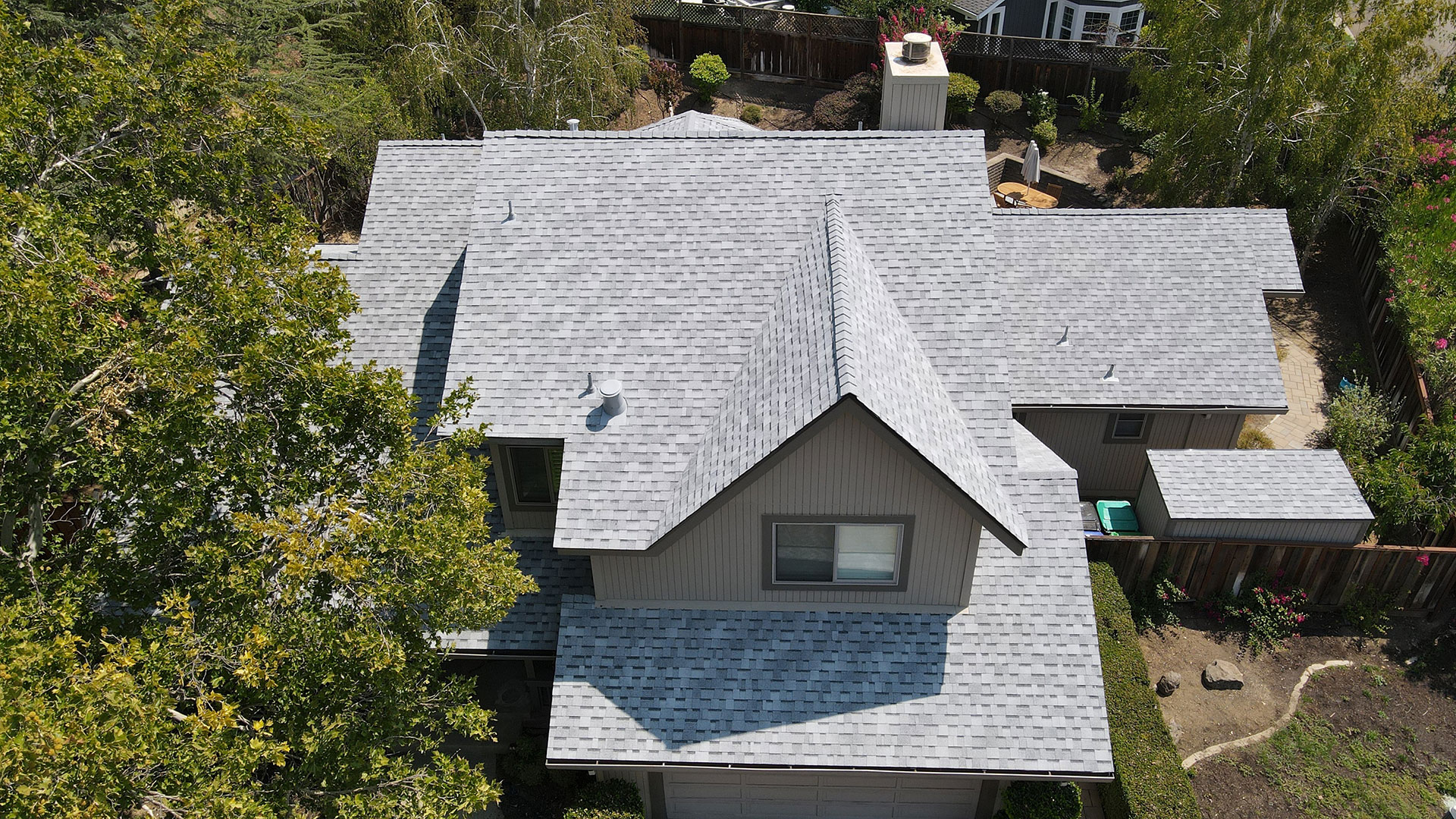 The image shows a house with a gray roof and multiple windows, set against a background that includes trees and a clear sky.